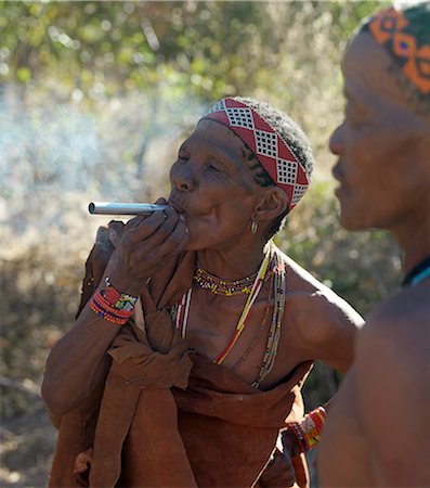 simsearch:862-03820241,k - A woman of the NIIS hunter gatherer band enjoys a smoke during a break in foraging for food.The NIIS are a part of the San people, often referred to as Bushmen.They differ in appearance from the rest of black Africa having yellowish skin and being lightly boned, lean and muscular. Stock Photo - Rights-Managed, Code: 862-03820239