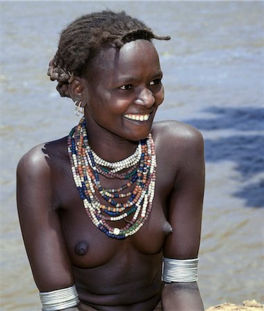 simsearch:862-03711116,k - A young Daasanech girl beside the Omo River. Her hairstyle, necklaces and metal armbands are typical of her tribe.The Dassanech people live in the Omo Delta of southwest Ethiopia, one of the largest inland deltas in the world. Foto de stock - Con derechos protegidos, Código: 862-03820347