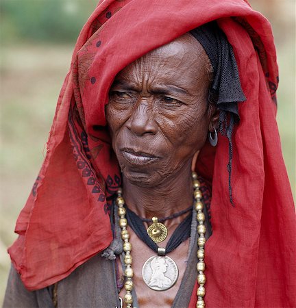 simsearch:862-03820241,k - An old Oromo woman wears a brass necklace and pendant, and a silver pendant made from a Maria Theresa thaler, an old silver coin minted in Austria, which was widely used as currency in northern Ethiopia and Arabia until the end of World War II. With a bright red headscarf, She was on her way to Senbete, an important weekly market close to the western scarp of the Abyssinian Rift. Stock Photo - Rights-Managed, Code: 862-03820398