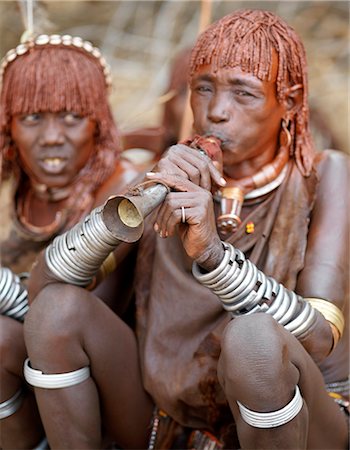 simsearch:862-03820649,k - A Hamar woman blows a tin trumpet at a Jumping of the Bull ceremony.The Hamar are semi nomadic pastoralists of Southwest Ethiopia whose women wear striking traditional dress and style their red ochred hair mop fashion.The Jumping of the Bull ceremony is a rite of passage for young men. Stock Photo - Rights-Managed, Code: 862-03820510