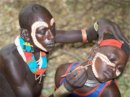 simsearch:862-03711116,k - A Hamar man with an unusual hairstyle decorates a girls face before the start of a Jumping of the Bull ceremony.The semi nomadic Hamar of Southwest Ethiopia embrace an age grade system that includes several rites of passage for young men.After the ceremony, the initiate attains full manhood and is permitted to marry. Foto de stock - Con derechos protegidos, Código: 862-03820520