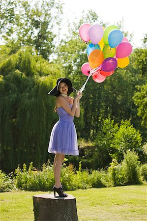 simsearch:877-06834306,k - Young woman holding bunch of balloons, standing on tree stump Stock Photo - Rights-Managed, Code: 877-06834292