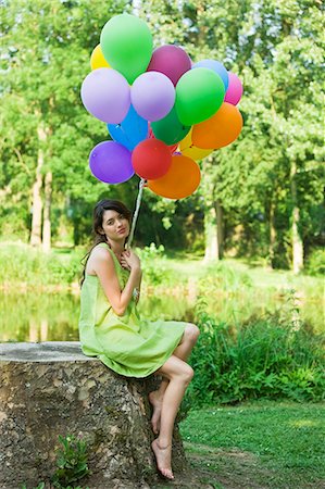 simsearch:877-06834306,k - Young woman holding bunch of balloons, sitting on tree stump Stock Photo - Rights-Managed, Code: 877-06834307