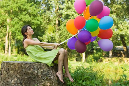 simsearch:877-06834306,k - Young woman holding bunch of balloons, sitting on tree stump Stock Photo - Rights-Managed, Code: 877-06834310