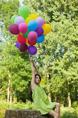 simsearch:877-06834306,k - Young woman holding bunch of balloons, sitting on tree stump Stock Photo - Rights-Managed, Code: 877-06834311