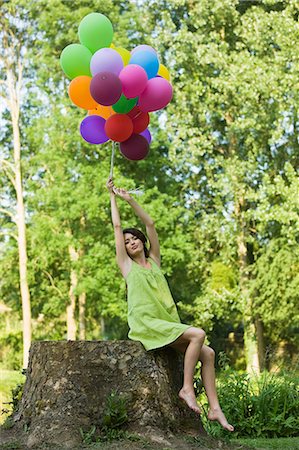 simsearch:877-06834306,k - Young woman holding bunch of balloons, sitting on tree stump Stock Photo - Rights-Managed, Code: 877-06834312