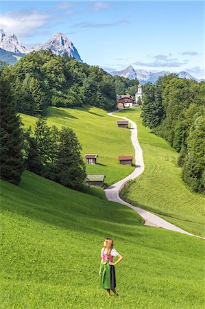 A girl in Typical Bayern dress walking in front of Wamberg village, with Mount Zugspitze and Waxenstein on the background. Garmisch Partenkirchen, Bayern, Germany. Stock Photo - Rights-Managed, Code: 879-09100954