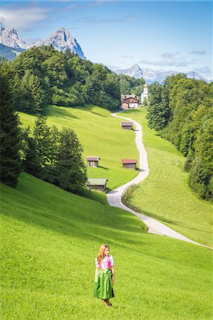 A girl in Typical Bayern dress walking in front of Wamberg village, with Mount Zugspitze and Waxenstein on the background. Garmisch Partenkirchen, Bayern, Germany. Stock Photo - Rights-Managed, Code: 879-09100953