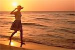 Silhouette de femme qui marche sur la plage au coucher du soleil