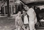 Portrait of Family Sitting on Car Near House