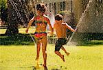 Back View of Boy and Girl in Swimwear, Playing In Sprinkler