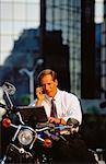 Businessman Using Cellular Telephone and Laptop Computer on Motorcycle