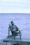 Man Sitting in Chair on Dock with Book