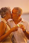 Mature Couple Kissing on Beach Holding Drinks
