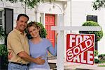 Portrait de Couple devant la maison avec le signe vendu