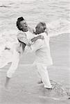 Mature Couple Embracing in Surf On Beach