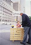 Boy with Lemonade Stand on Street Serving Businessman