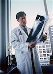 Male Doctor Standing near Window Looking at X-Ray in Office