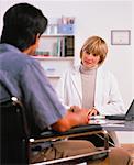 Female Physiotherapist Consulting With Male Patient in Wheelchair