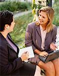 Businesswomen Sitting on Bench With Laptop and Agenda Outdoors