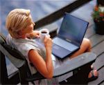 Woman Sitting in Adirondack Chair On Deck, with Laptop and Mug