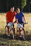 Porträt des Paares mit dem Mountainbike in Feld von hohem Gras