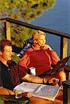 Mature Couple Sitting in Chairs On Deck with Newspaper and Laptop