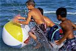 Trois garçons en maillot de bain, jouer avec le ballon de plage dans l'eau sur la plage