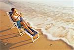 Mature Woman Sitting in Chair on Beach Using Electronic Organizer