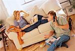 Couple Relaxing at Home with Woman on Sofa and Man Using Phone