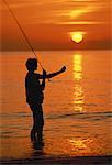 Silhouette de femme de pêche sur la plage au coucher du soleil