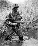 Soldier Wearing Camouflage Wading through Water with Weapon