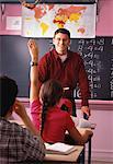 Male Teacher Looking at Girl with Hand Raised in Classroom