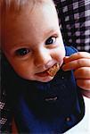 Close-Up of Baby Sitting in High Chair, Eating Cookie