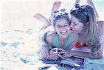 Mother and Daughter in Swimwear Lying on Beach with Magazine Laughing