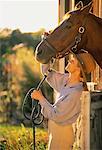 Woman Putting Reigns on Horse at Stable