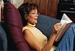 Mature femme assise sur le canapé lecture livre