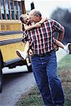 Grandfather Carrying Granddaughter near School Bus