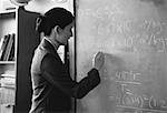 Female Teacher Writing on Blackboard in Classroom
