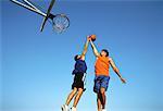 Two Men Jumping in Air, Playing Basketball Outdoors