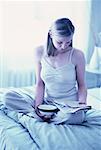 Femme assise sur le lit lisant journal, tenant bol