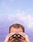 Man Looking through Binoculars With Dollar Signs and Sky