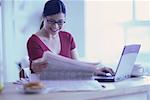 Woman Sitting at Desk with Laptop Computer and Newspaper