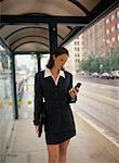 Businesswoman Standing in Bus Shelter, Holding Cell Phone