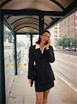 Businesswoman Standing in Bus Shelter, Using Cell Phone