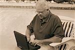 Homme d'âge mûr assis dans le fauteuil à l'aide d'ordinateur portable à l'extérieur