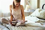 Femme assise sur le lit, lire le journal, tenant bol