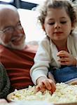 Grandfather and Granddaughter On Sofa with Bowl of Popcorn