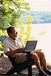 Man Sitting in Chair with Laptop Computer near Lake