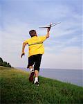 Back View of Boy Running through Field with Toy Airplane